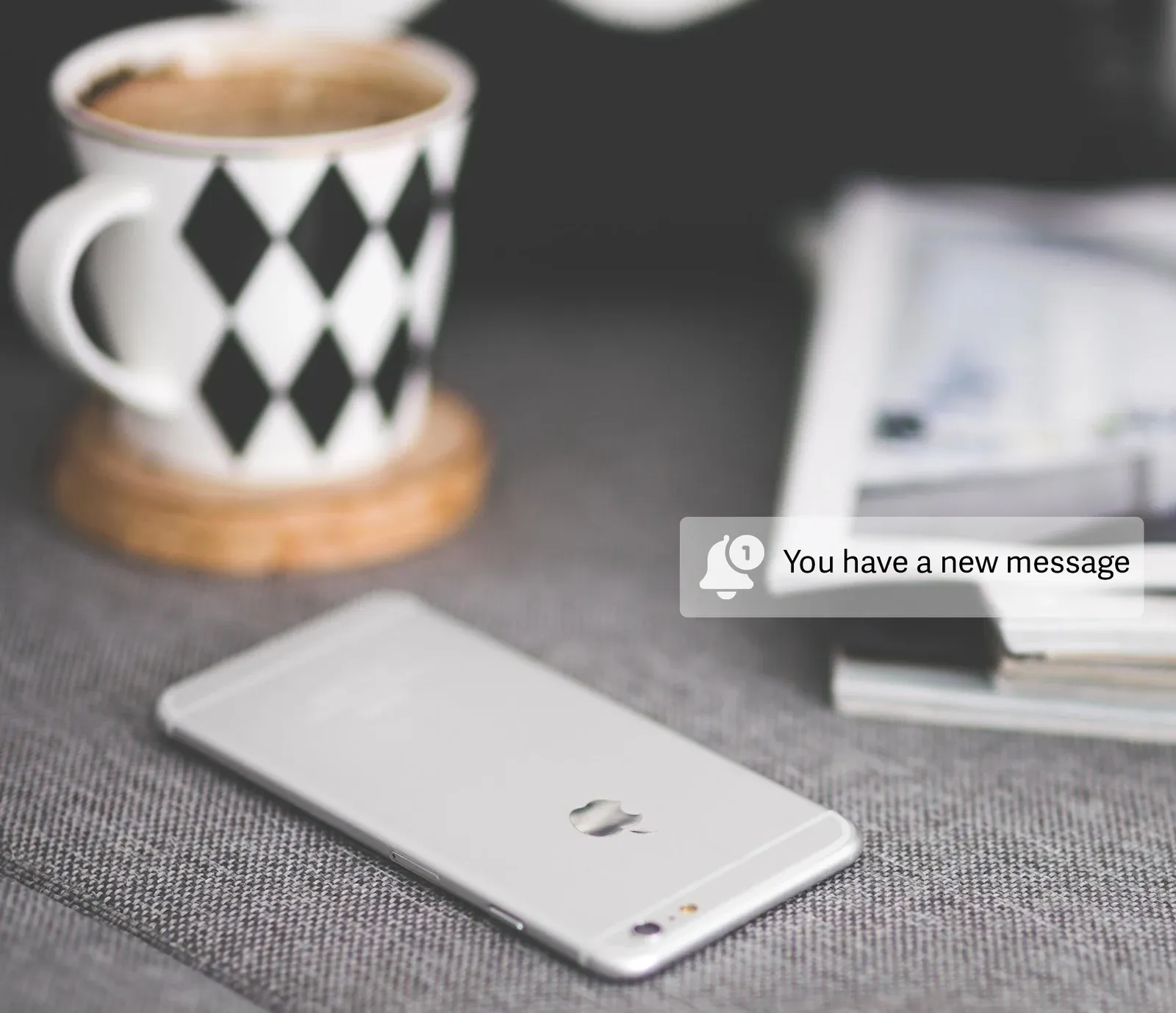 A phone on a table beside a coffee cup, with a “You have a new message” notification.